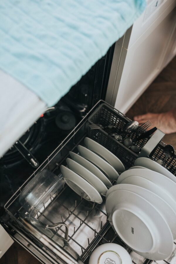An open dishwasher reveals clean white plates, bowls, and utensils neatly arranged in the lower rack, exemplifying simple hospitality etiquette.
