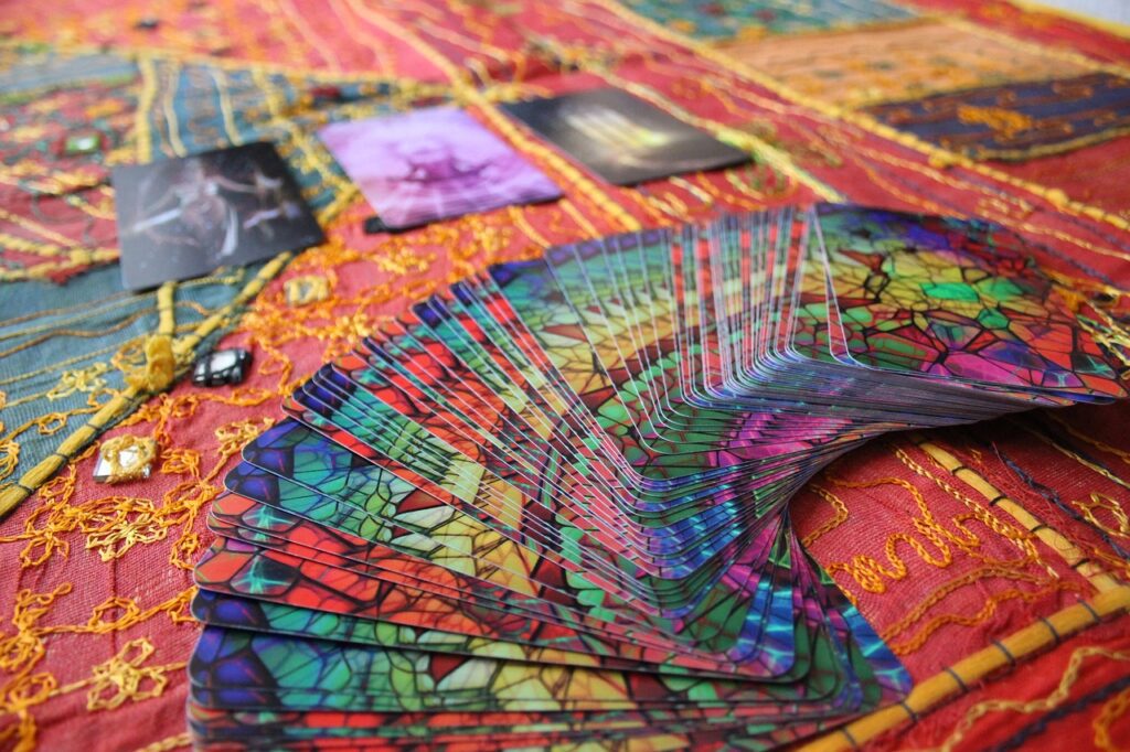 A spread of colorful tarot cards is laid out on a vibrant, embroidered fabric background, with a few gemstones placed nearby—perfect for adding a mystical touch to your Halloween dinner party.